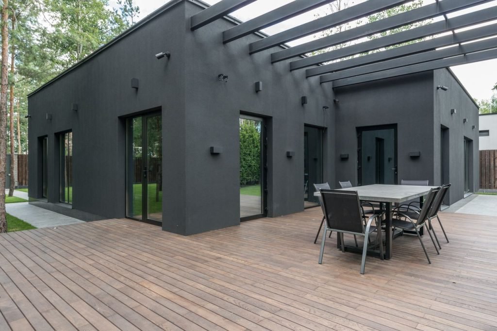 The Art of Drawing Readers In: Your attractive post title goes here Contemporary black house with spacious wooden terrace and outdoor seating area.